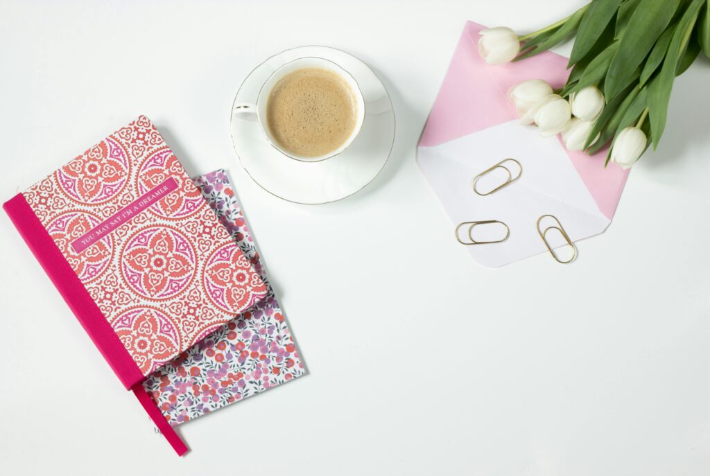 Flat lay of a stylish workspace featuring a coffee cup, tulips, and vibrant notebooks.